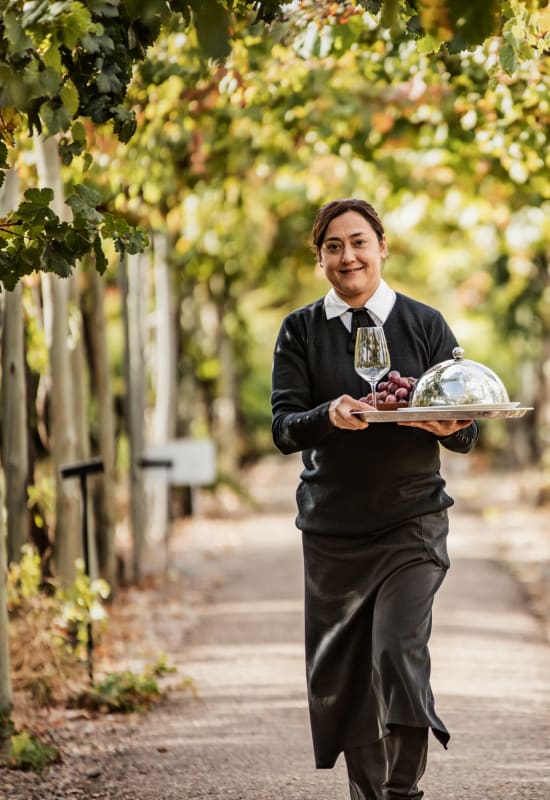 One of the hotel waiters carries a silver dish and wine glass through the lodge gardens.