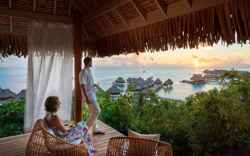 A young couple stand on their private veranda overlooking the incredible overwater bungalows.