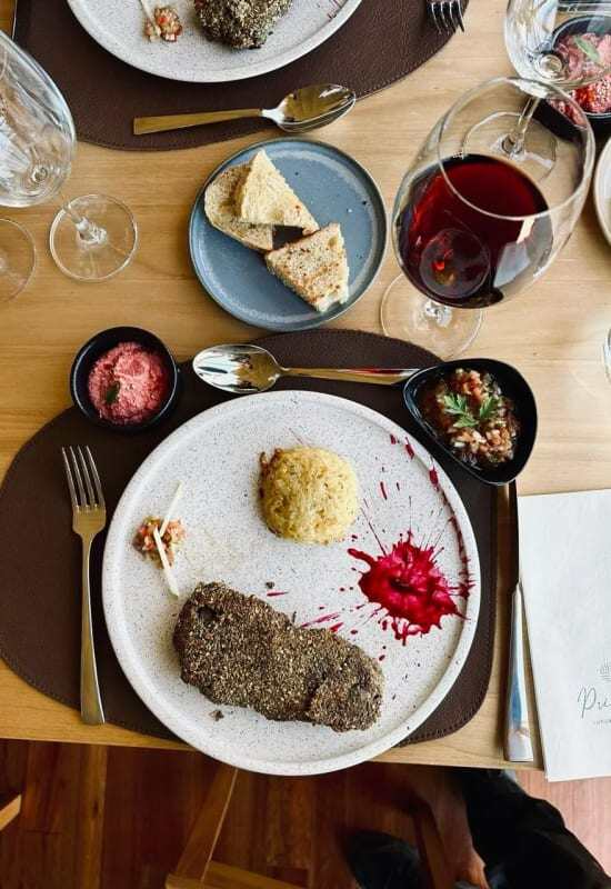 A dish of food displays michelin-style presentation, paired with a glass of red wine and a plate of bread.