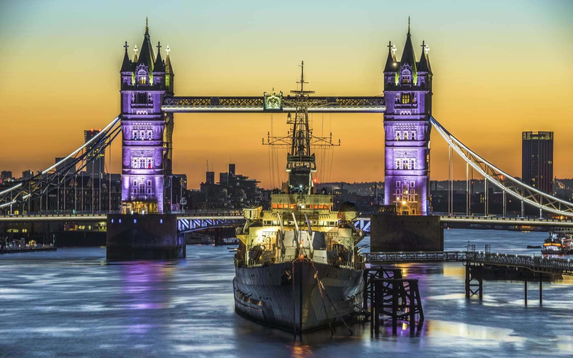 HMS Belfast sits ahead of Tower Bridge during sunset.