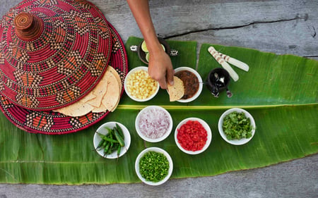 Bowls of chopped ingredients are placed on a leaf next to the flatbread. 