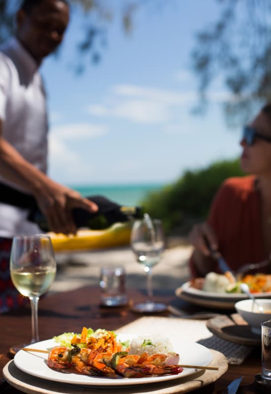 A dining table is full of plates with shrimp, and a waiter pours white wine into wine glasses. 