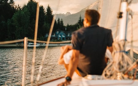 A man perches on the edge of a sailing boat out on the lake beside the lodge.