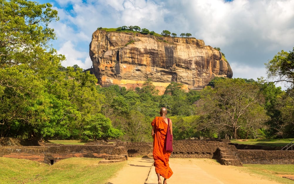 A local man in Buddhist dress wanders ahead of the gigantic Sigiriya Rock.