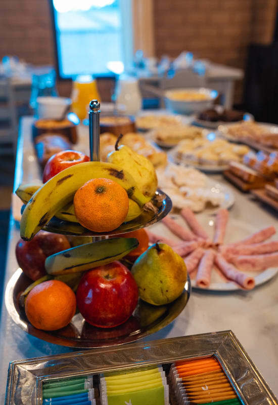 A silver plate of fruit is sat next to multiple plates of meats and other breakfast foods.