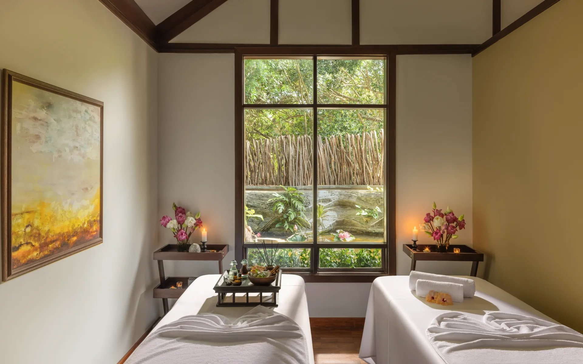 Two massage beds lay in a cosy room. A large window on-looks the surrounding jungle.