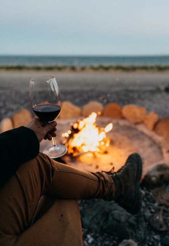 A guest enjoys a glass of red wine ahead of a burning log fire.