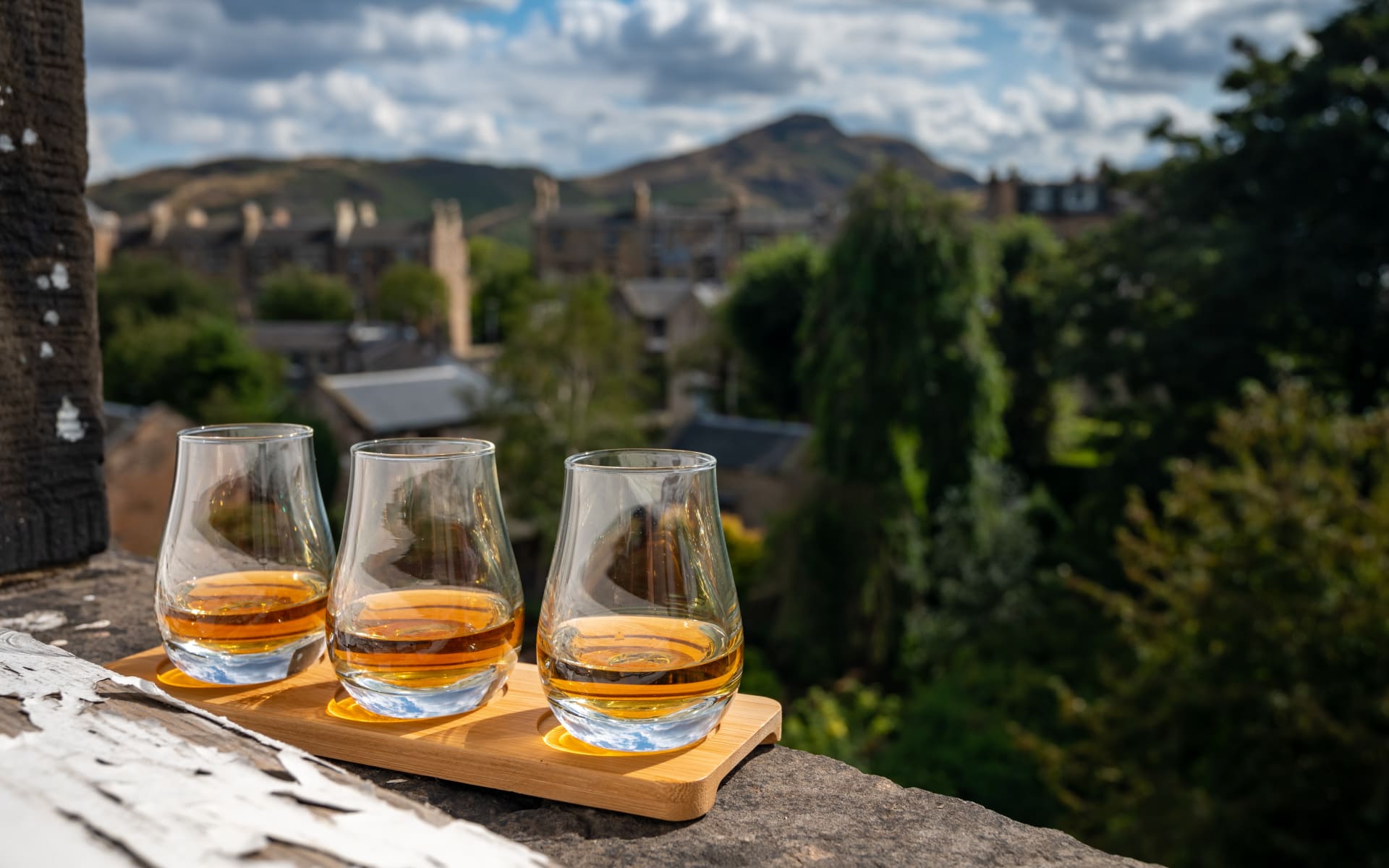 Three drams of whisky perch ahead of a green scenery.