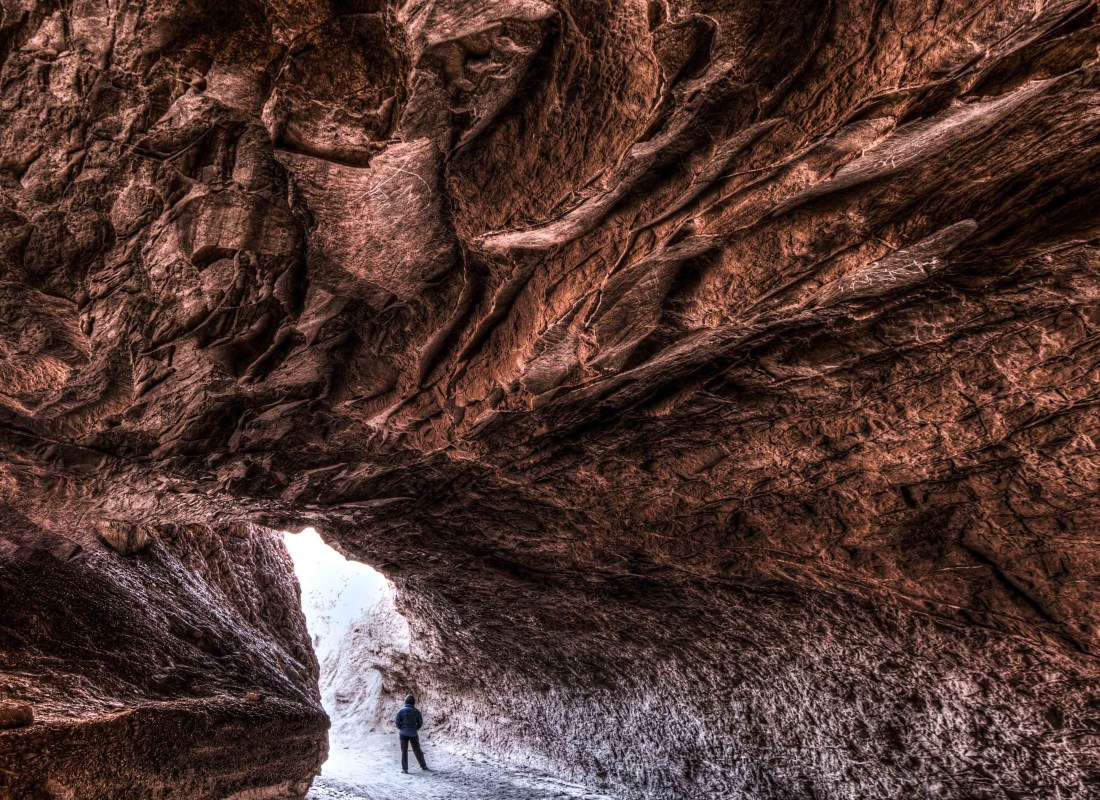 There is a man standing in the middle of a brown-red cave.