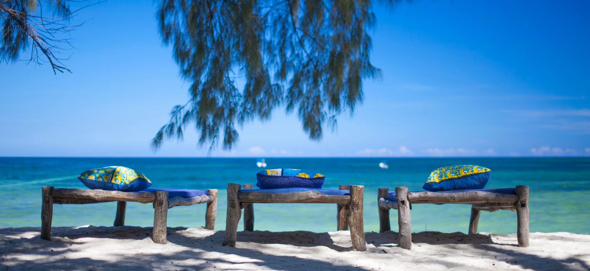 Three wooden sunloungers are sitting on white sand overlooking the ocean.