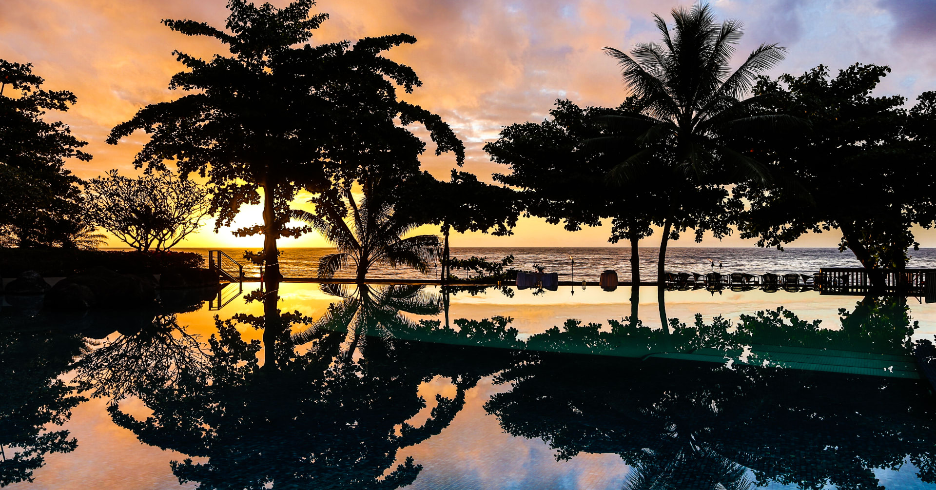 Sunset over palm trees which are reflecting onto swimming pool