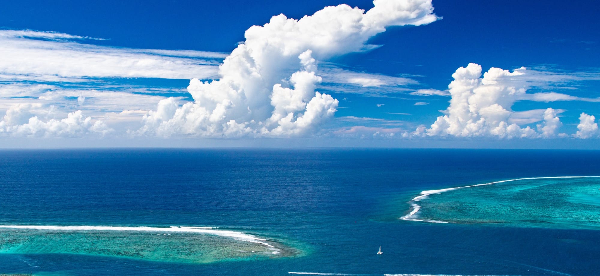 The blue ocean has pockets of turquoise waters and is under really white, fluffy clouds. 