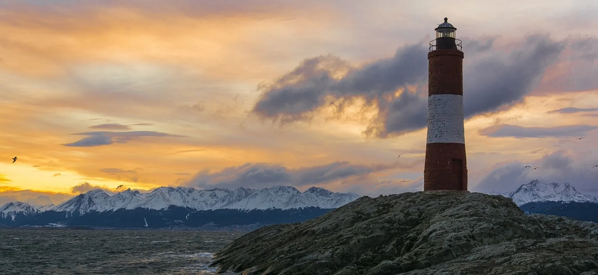 A lighthouse fronts snow-capped mountains in Ushuaia. 