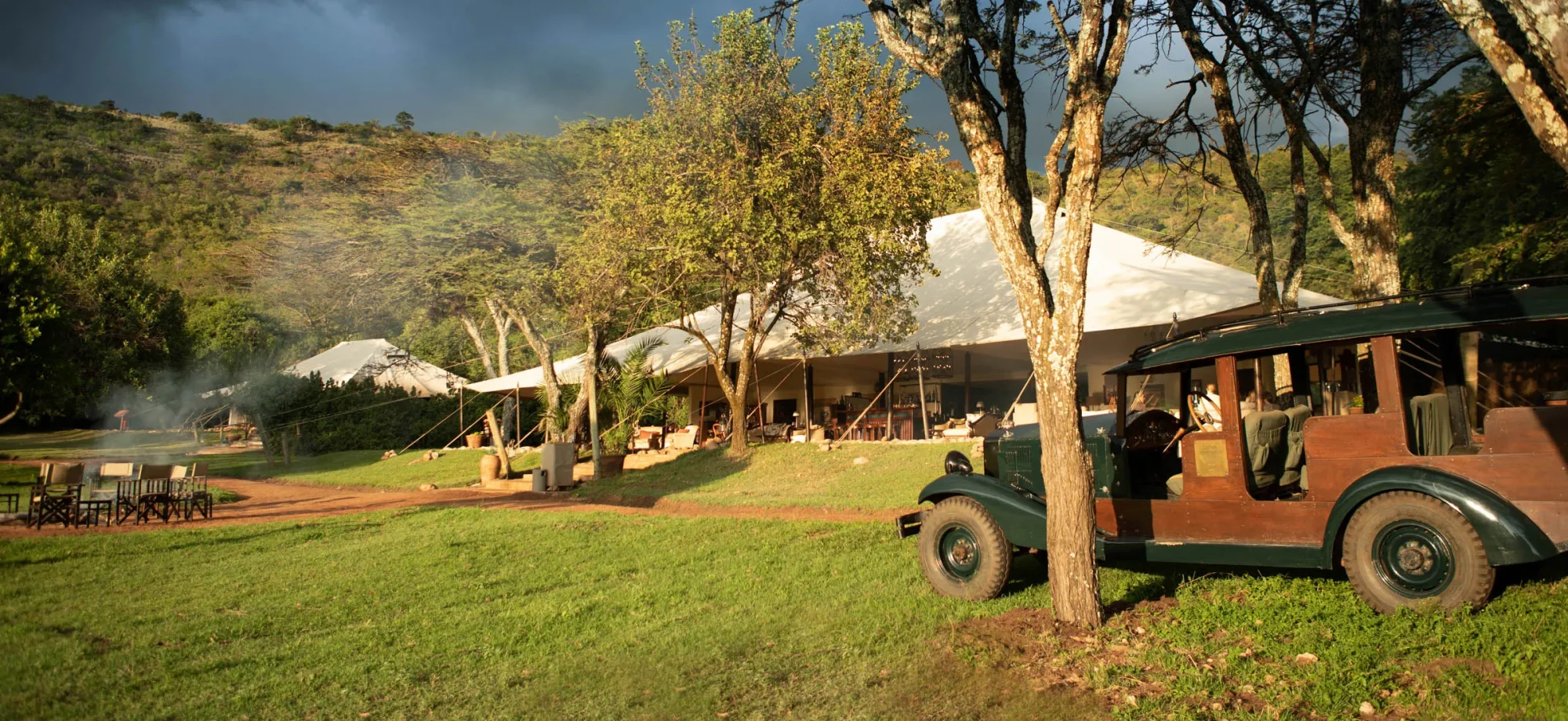 A game vehicle is parked outside the communal tent during daytime.