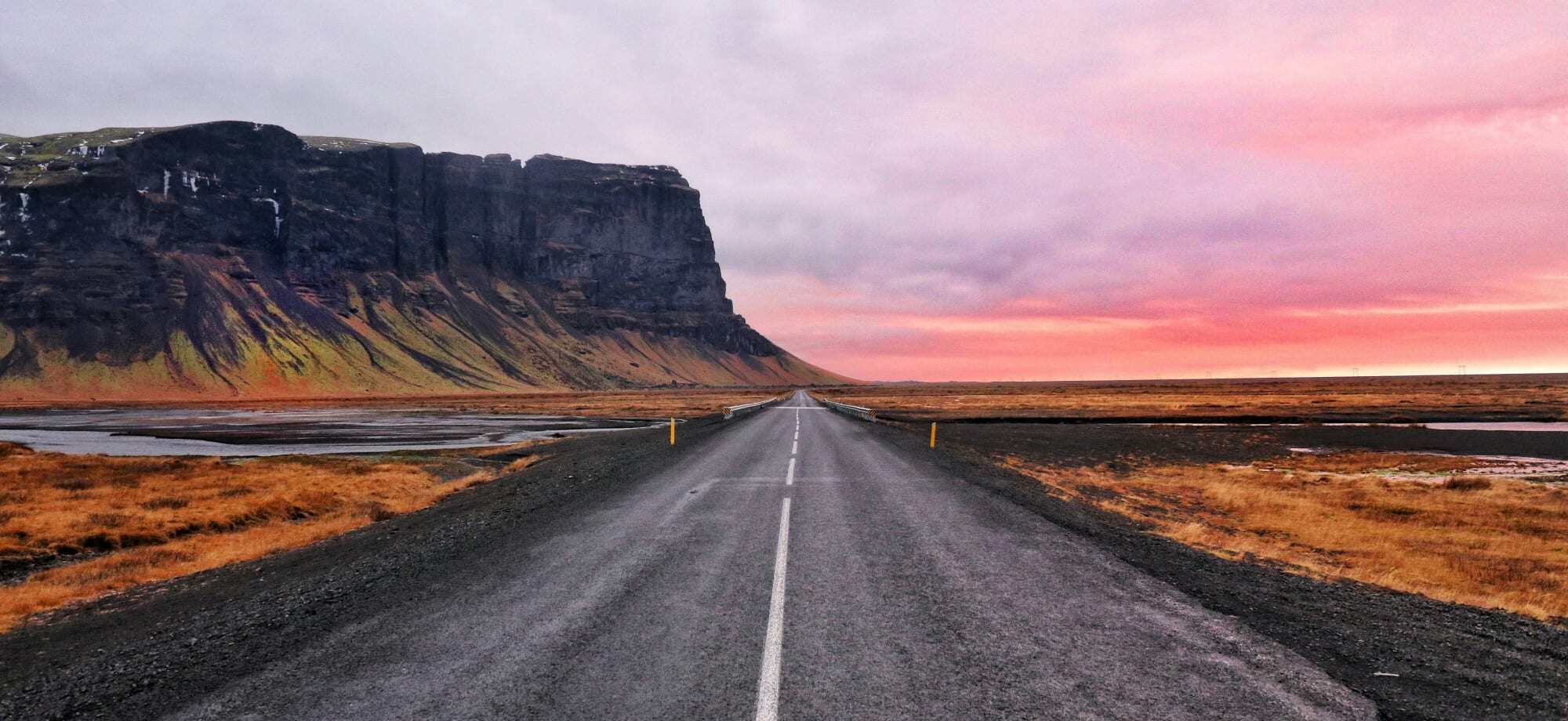 An ongoing, narrow road leads towards a sunset in Iceland.